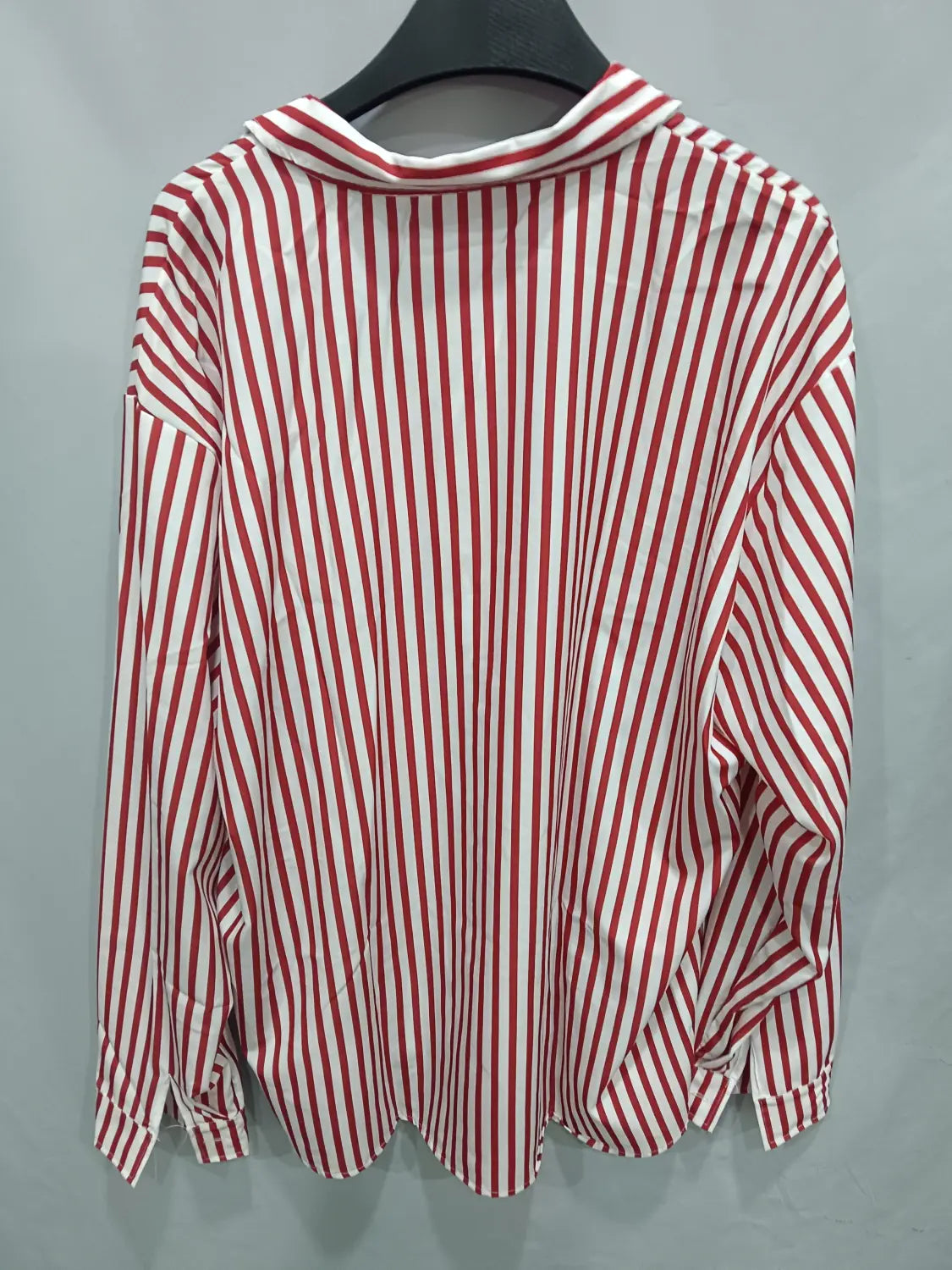 Chemise décontractée à manches longues rayée verticalement rouge et blanc pour hommes, avec un col posé sur un cintre noir.