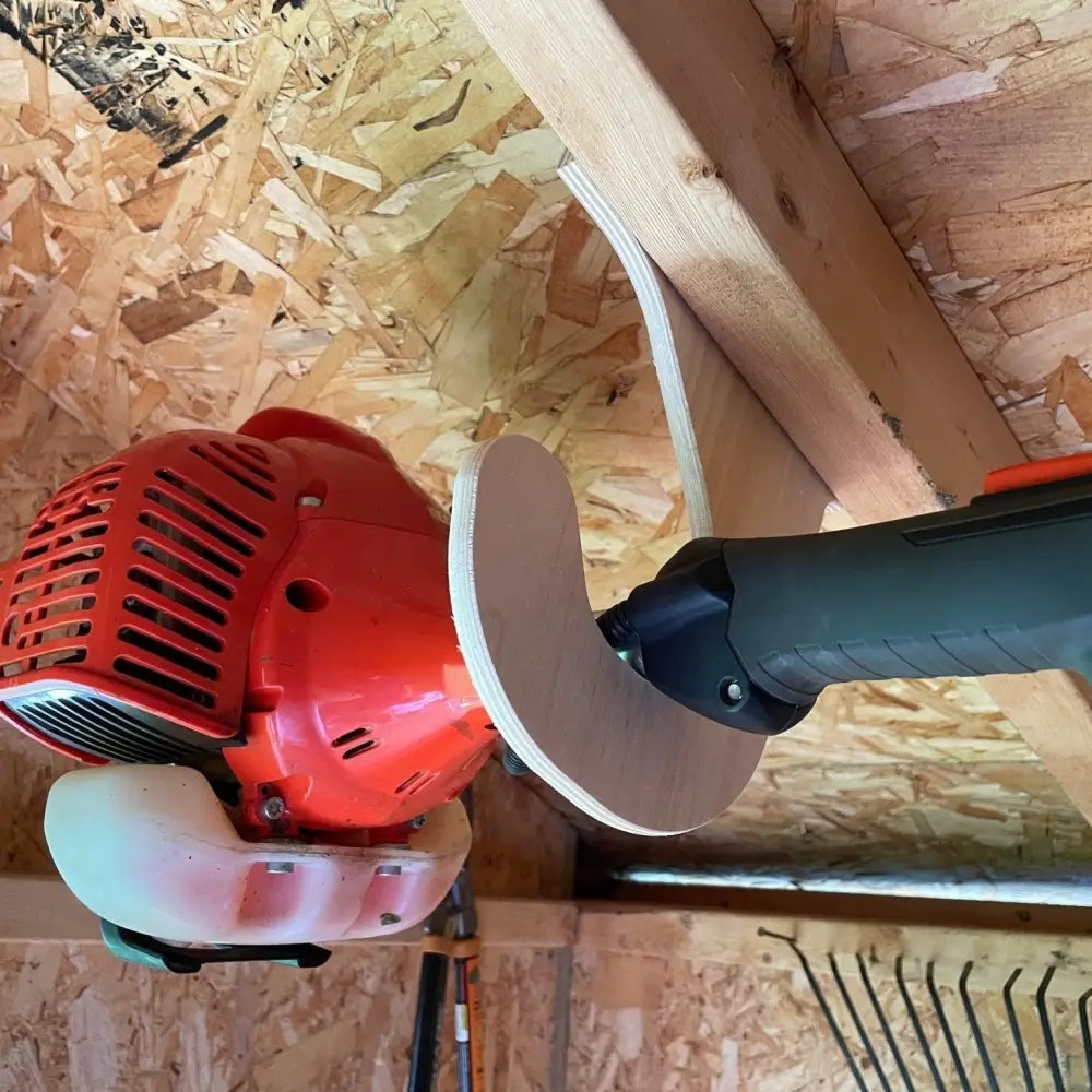Red and black gas-powered brush cutter with circular blade stored on ceiling mounted birch plywood weed wacker rack