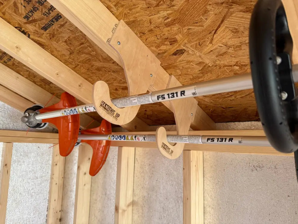 Two orange and silver fs 131 r string trimmers mounted on a ceiling mounted birch plywood weed wacker storage rack