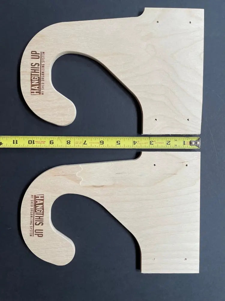 Light-colored birch plywood ceiling mounted weed wacker storage rack components with curved hooks and engraved branding