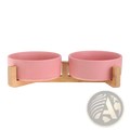 Pink ceramic double pet bowl mounted on a light wood stand for feeding cats or small dogs