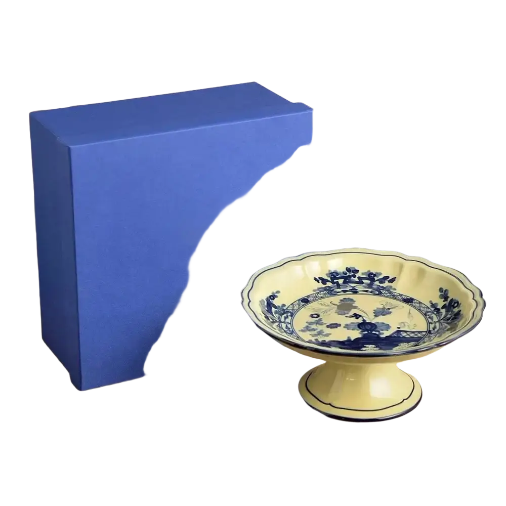 A cream-colored ceramic pedestal dish with blue floral patterns and scalloped rim from a ceramic floral tableware set