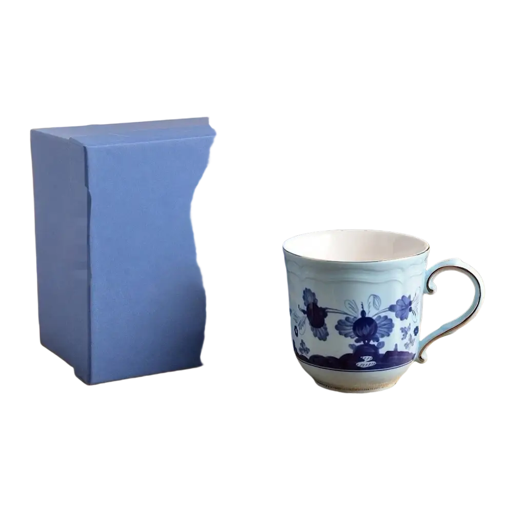 A delicate light blue ceramic coffee mug with dark blue floral patterns displayed beside a solid blue gift box