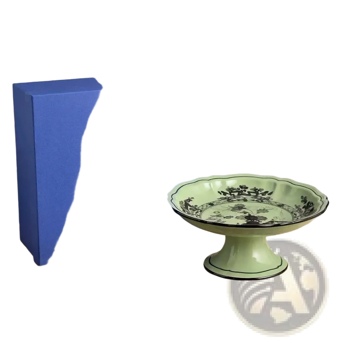 A delicate mint green ceramic dessert bowl with fluted rim and black floral pattern beside royal blue gift box
