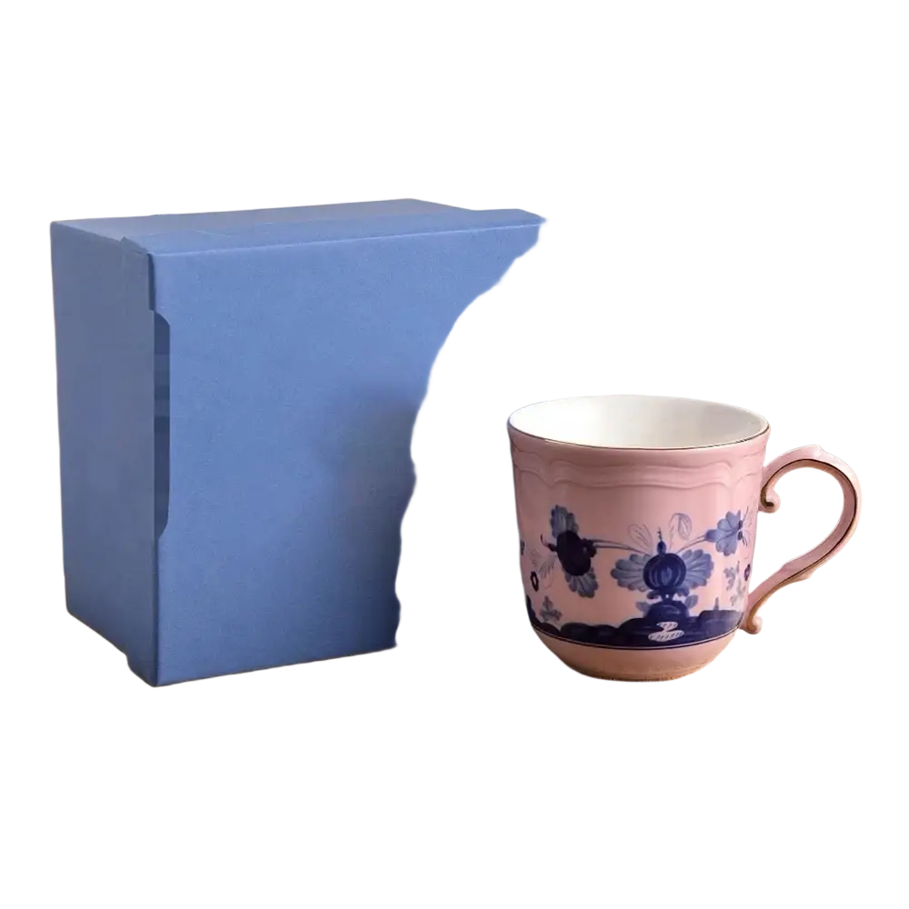 A delicate pink ceramic coffee mug with intricate blue floral patterns and matching handle from a floral tableware set
