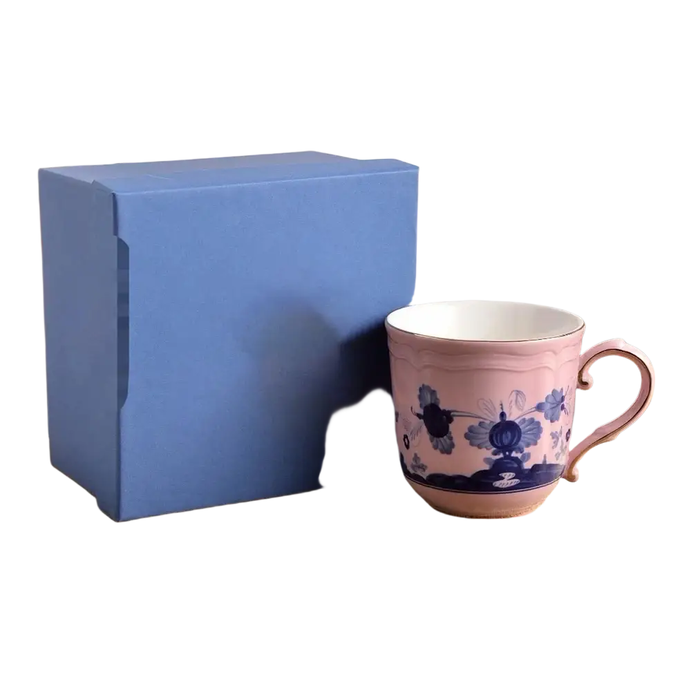 A delicate pink ceramic coffee mug with intricate blue floral patterns and matching handle in a floral tableware set