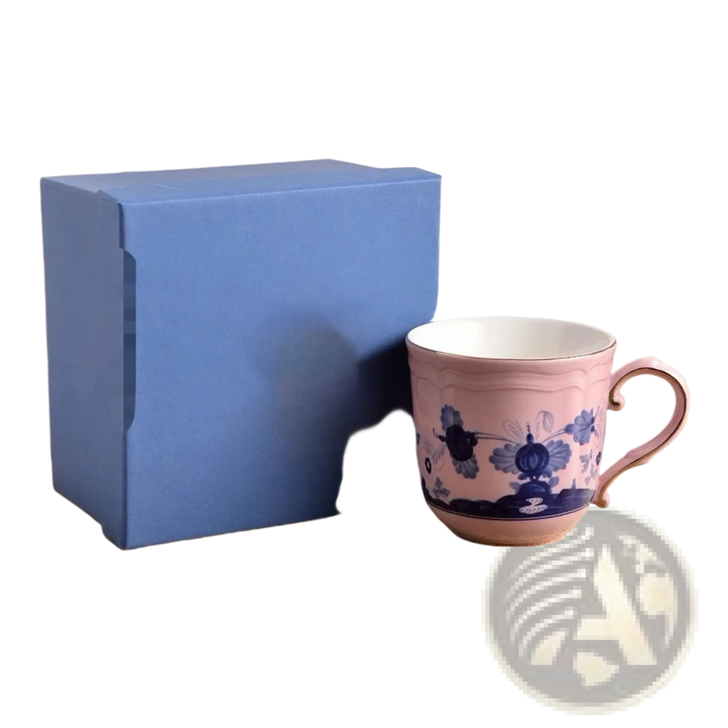 A delicate pink ceramic coffee mug with intricate blue floral patterns and matching handle in a floral tableware set