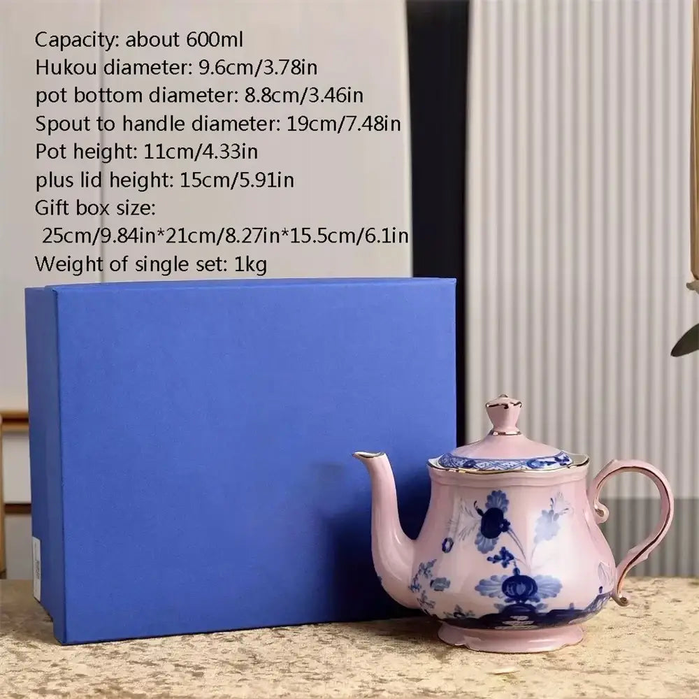 A delicate pink porcelain teapot with blue floral patterns and gold-trimmed edges from a ceramic floral tableware set