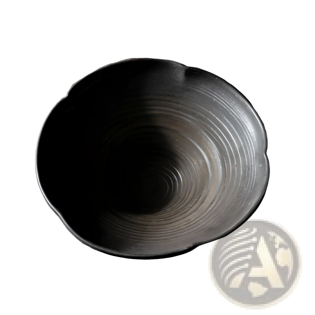 A dark gray ceramic lace fruit plate with a scalloped rim and concentric ridges on an aged wooden surface