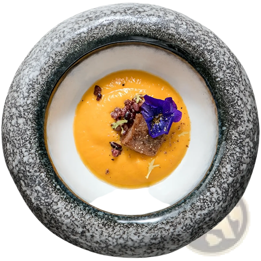 Ceramic sashimi bowl with retro speckled gray exterior and white interior holding orange soup garnished with flower and crumbles
