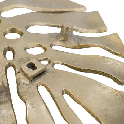 Antique brass-colored metal gold monstera leaf wall decor with intricate leaf-like cutouts and a small keyhole for hanging.