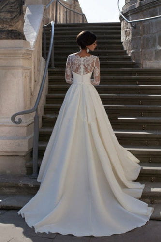 a flowing ivory wedding dress showing the back side with a lace back and long sheer sleeves suitable for formal occasions