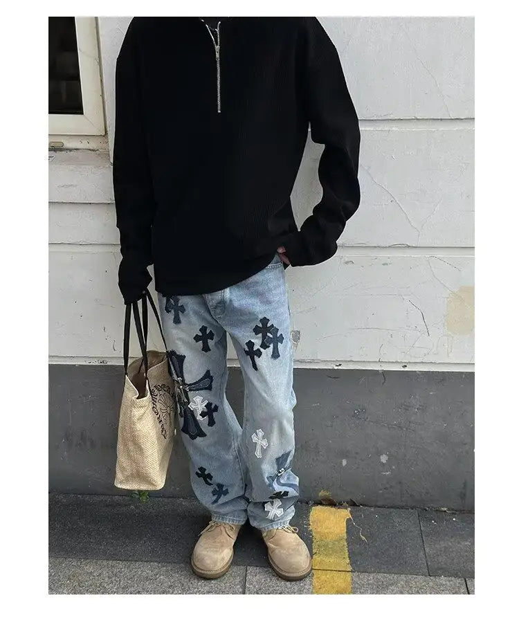 Sudadera tipo jersey acanalada de media cremallera para hombre combinada con jeans de mezclilla de lavado claro que presentan cruces bordadas en negro y blanco.