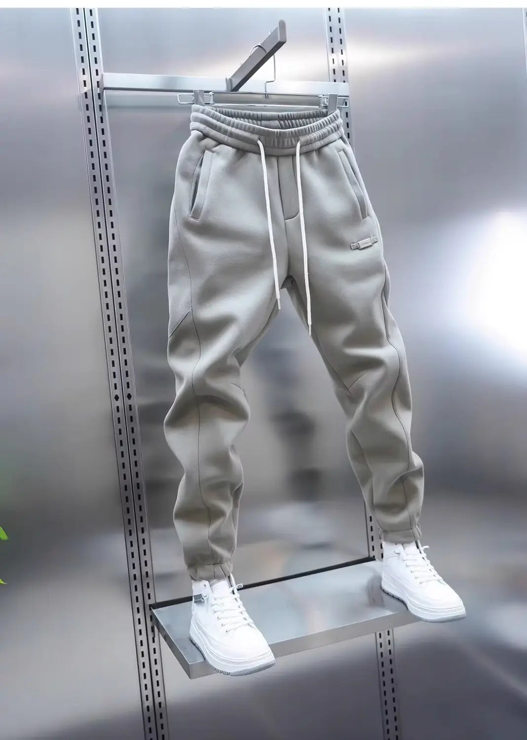 Mens casual solid color sweatpants in gray featuring white drawstrings and a small logo on the thigh hanging from a metal rack.