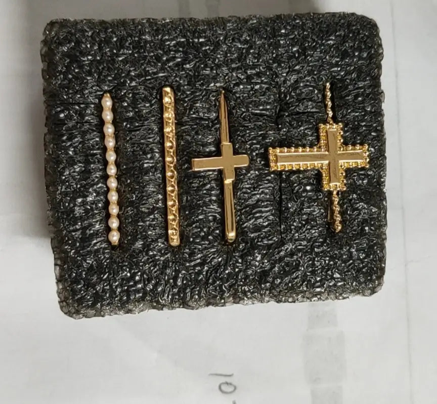 set of four gold-toned cross and beaded bar earrings displayed on black textured foam backing from gold embellished silicone strap decorative ring set