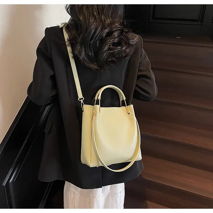 Cream-colored minimalist leather bucket bag with top handles and a detachable shoulder strap.