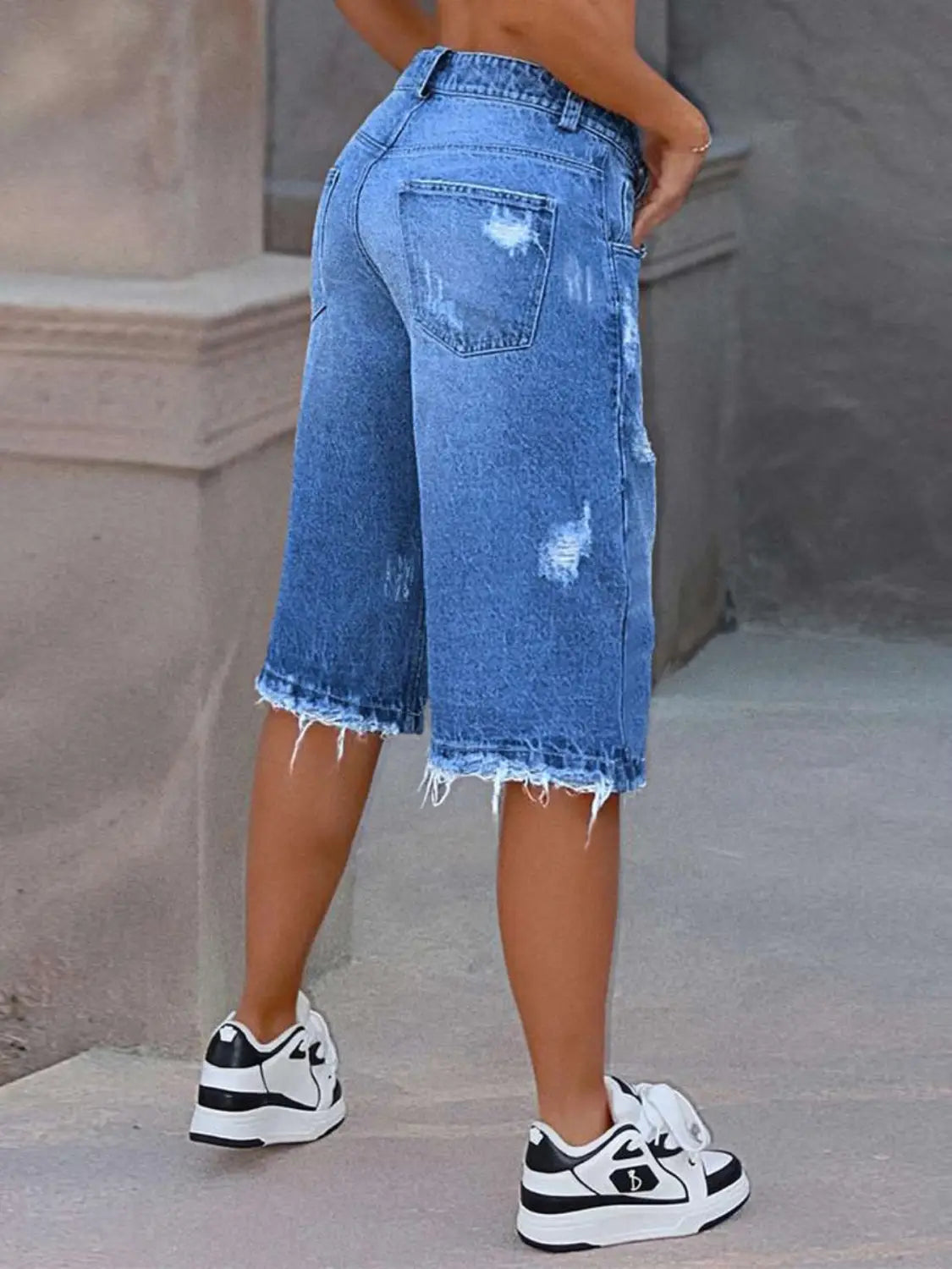 Pantalones capri de mezclilla azul desgastada con desgarros que muestran el reverso, con dobladillo deshilachado y bolsillos traseros clásicos.