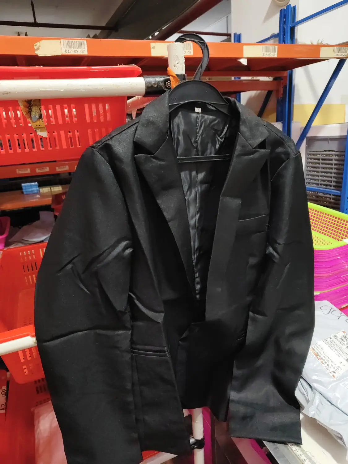 Veste de blazer décontractée à simple boutonnage bleu marine pour homme en satin noir, avec revers à encolure crantée et deux poches avant, suspendue sur un cintre noir