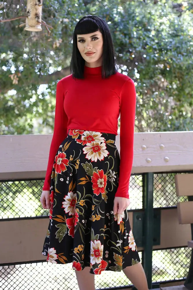 A woman wears a red long-sleeved turtleneck with a charlotte black floral 1950s vintage style circle skirt
