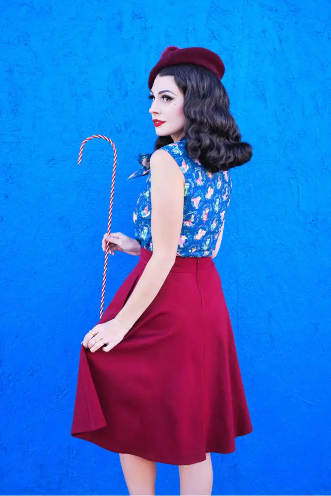 A woman wearing a charlotte burgundy plus size high waist circle skirt paired with a blue floral sleeveless top and red beret