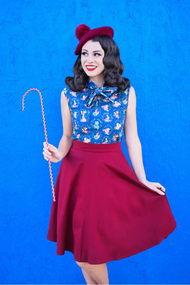 A woman wears a festive blue sleeveless top with bow and a Charlotte Burgundy plus size high waist circle skirt with red beret