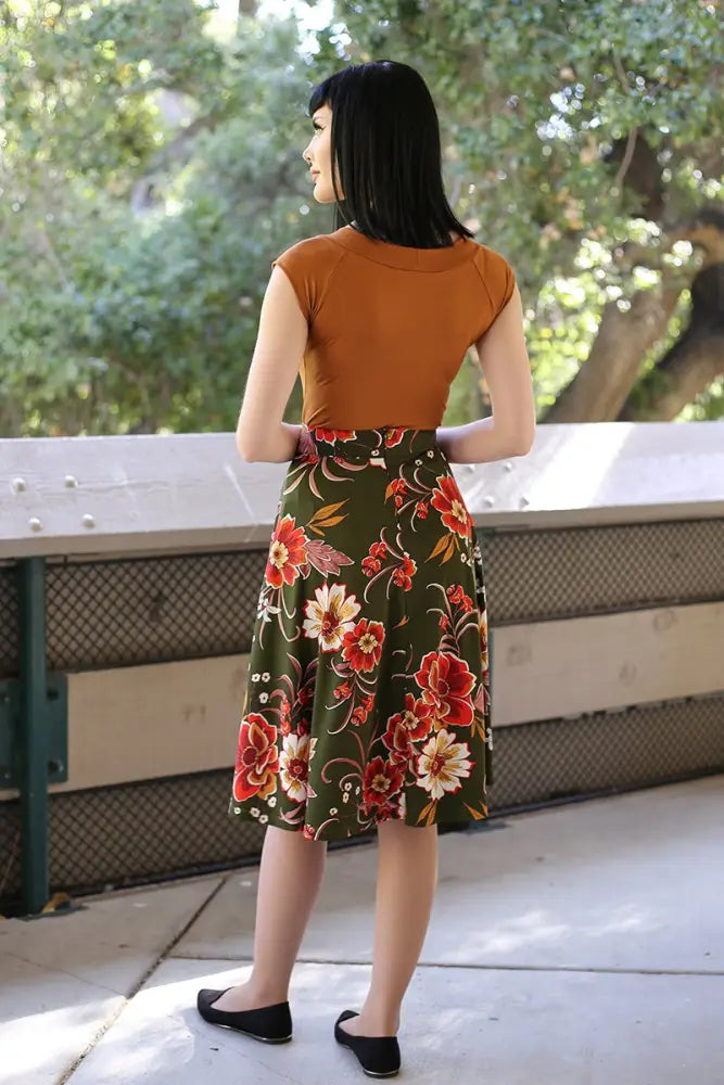 A woman wears the charlotte vintage green floral knit circle skirt with pockets featuring bold red and orange blossoms