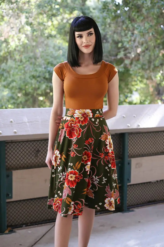 A woman wearing the Charlotte vintage green floral knit circle skirt with pockets featuring bold red pink and white flowers