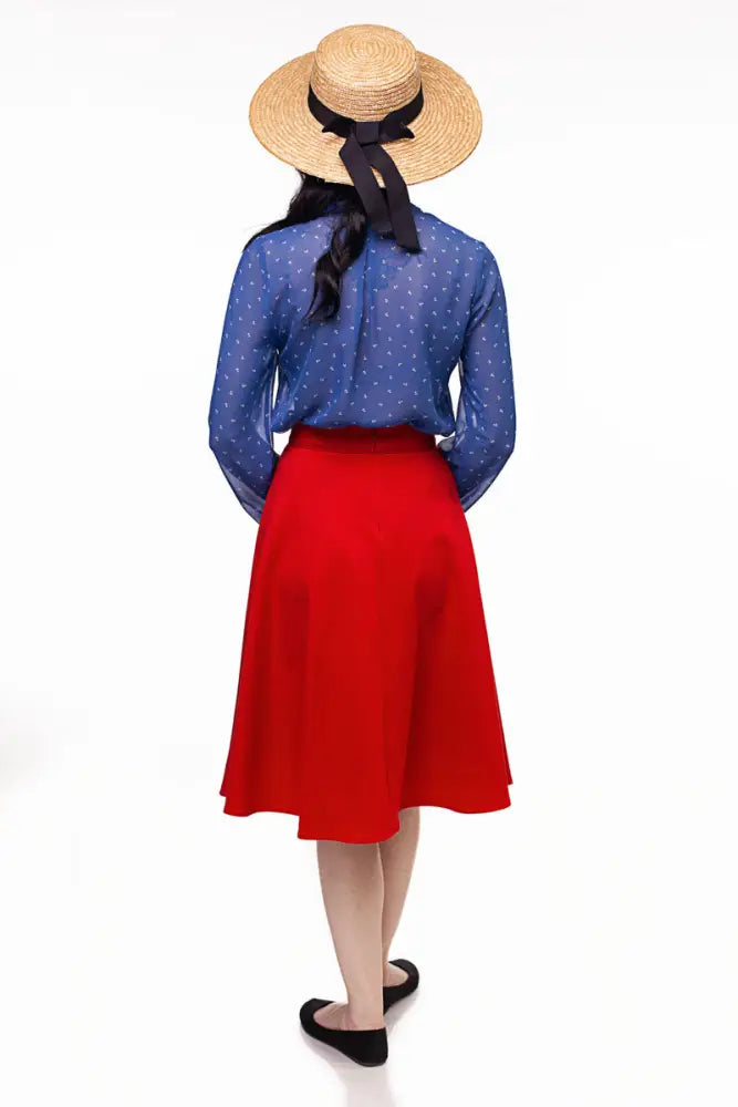 A woman seen from the back wears a wide-brimmed straw hat with a black ribbon and a charlotte red vintage high waisted circle skirt with pockets