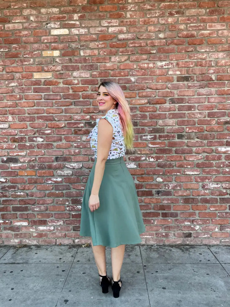 A woman wears a sleeveless white floral blouse with an olive green Charlotte Sage plus size vintage a line circle skirt
