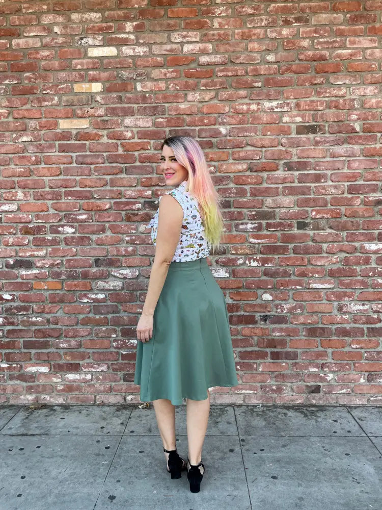 A woman wears a sleeveless white lace top with an olive green charlotte sage plus size vintage a line circle skirt