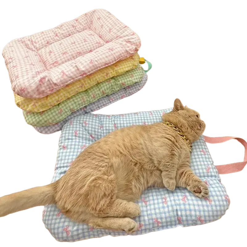 A fluffy orange cat lounges on a light blue and white gingham cotton checkered bow pet bed with pink strap