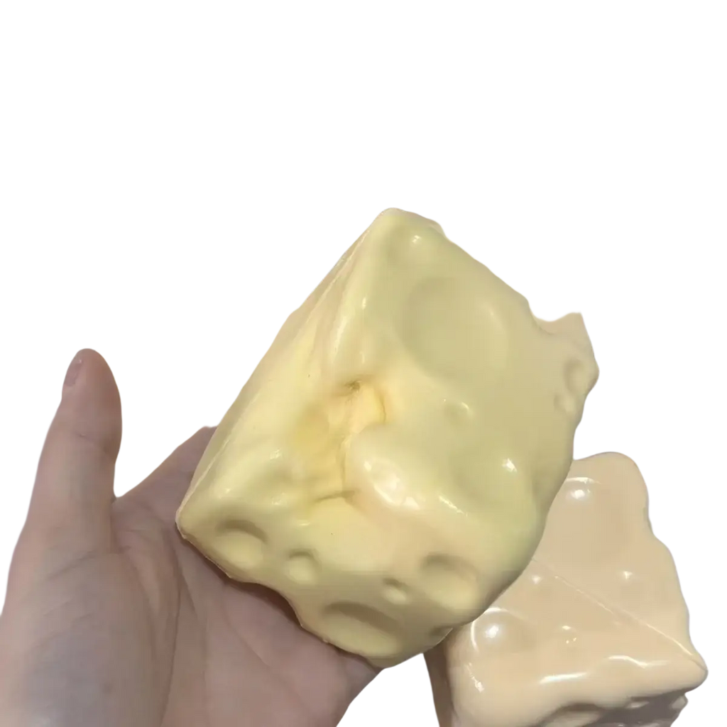A pale yellow glossy cheese cube stress ball soap with textured holes designed as a cube stress ball sensory toy