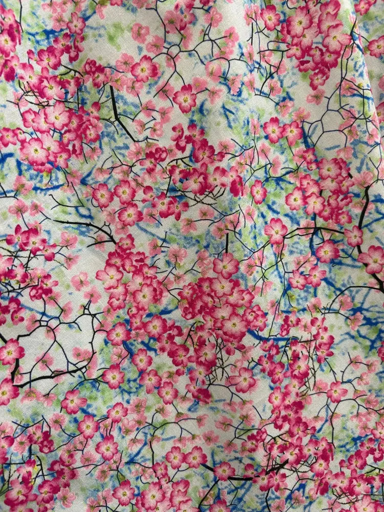 Pink cherry blossom patterned cotton flutter dress with black branches and blue accents on a light background