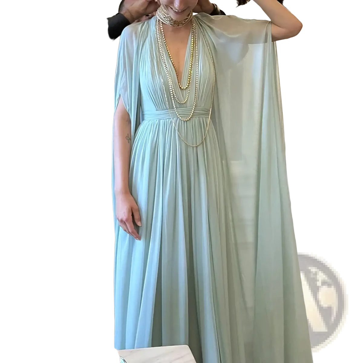 A flowing mint green chiffon cape evening dress with a draped cape and layered gold beaded necklaces