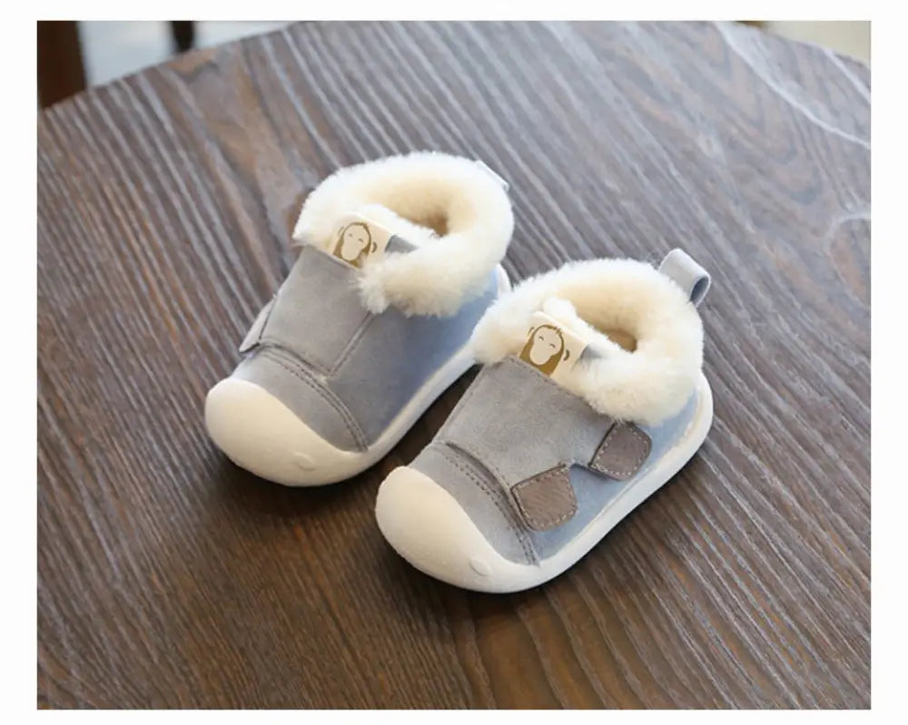 Light blue suede toddler snow boots with plush white faux fur lining and gold-tone monkey charm on the strap