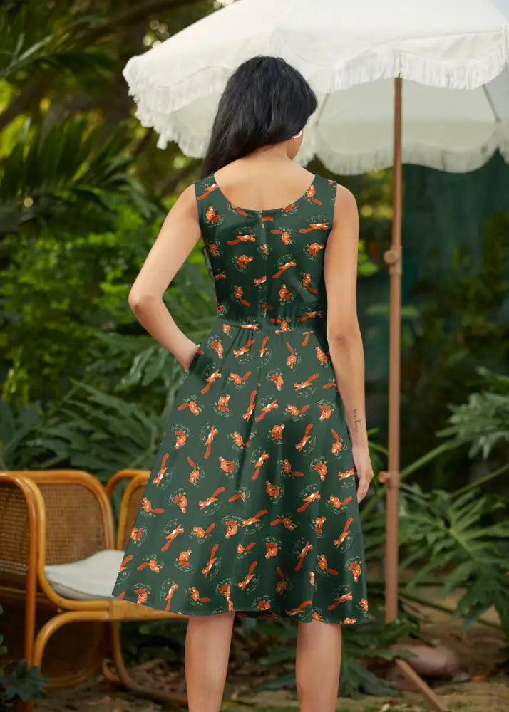A sleeveless dark green cotton midi fit and flare dress with orange fox and foliage pattern and pockets