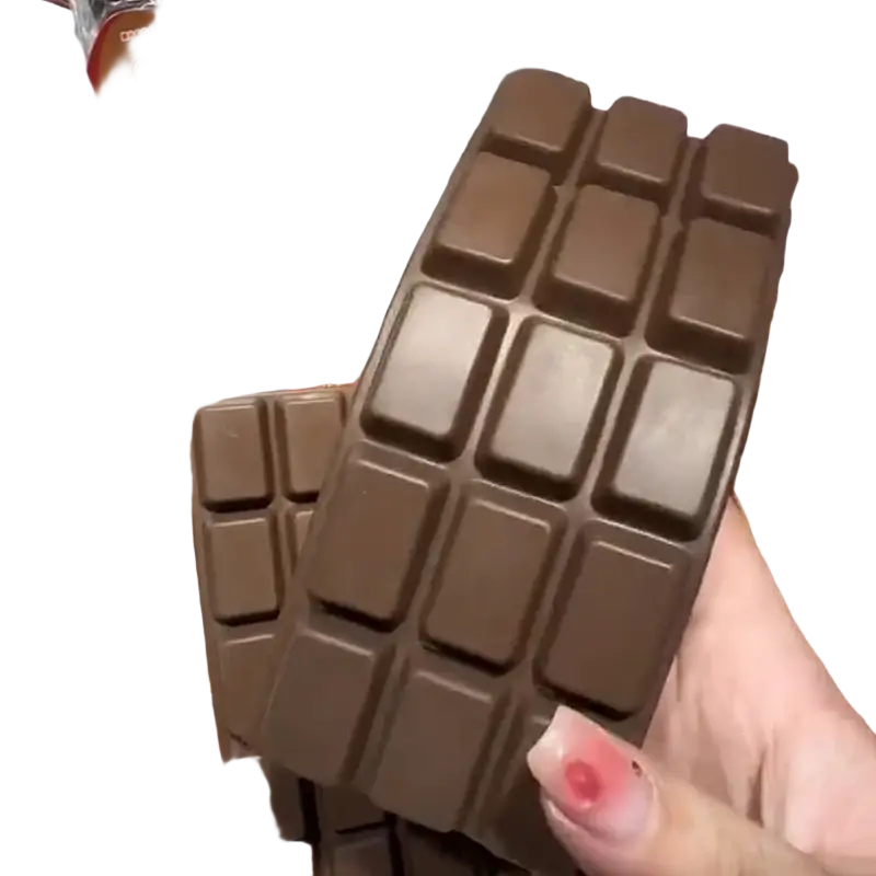 A hand holds a dark brown soft-textured chocolate bar squeeze toy with square segments for slow rising sensory fidget
