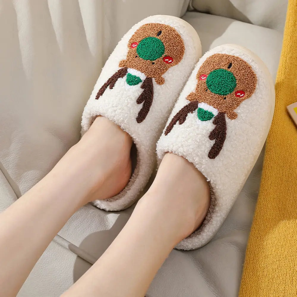 Cream-colored plush reindeer slippers with embroidered faces green noses brown antlers red cheeks and cozy faux fur lining
