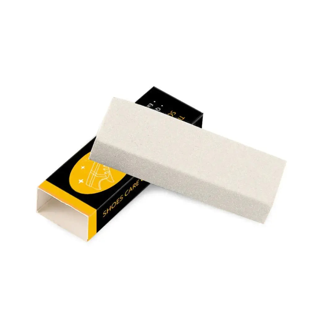 A rectangular off-white suede and leather shoe scuff eraser block with textured surface on black and yellow shoes care packaging