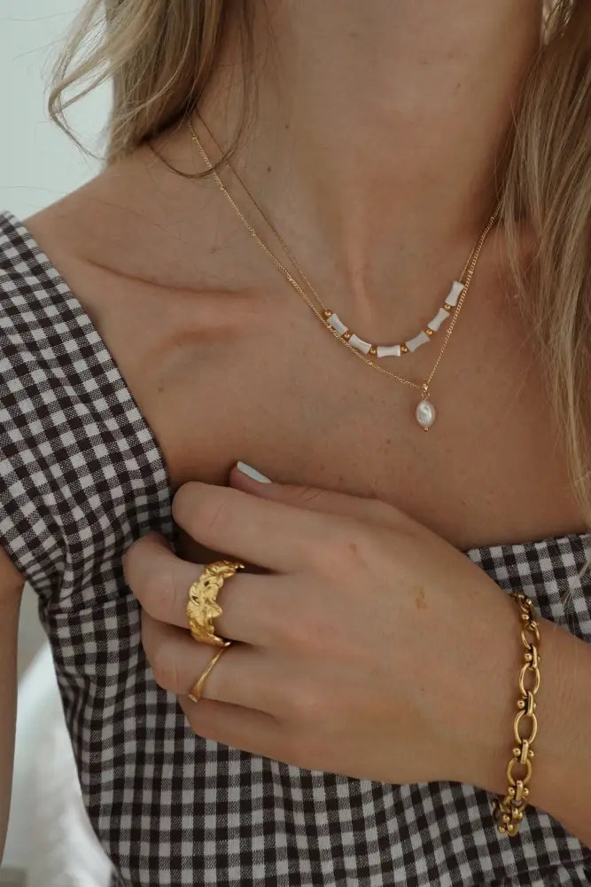 Cleo gold interlocking oval link chain bracelet featuring a gold-toned layered necklace with white beads and a pearl pendant