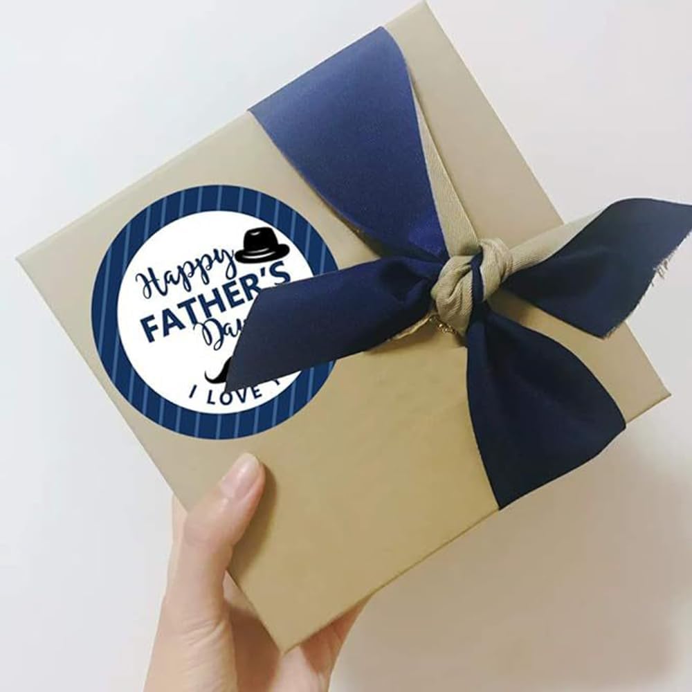 A beige gift box wrapped with a navy blue satin ribbon and a circular happy fathers day sticker from the fathers day gift stickers roll.
