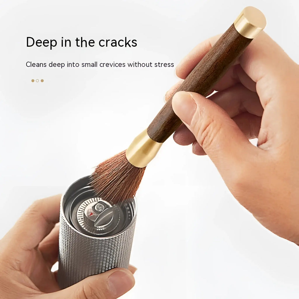 A sleek silver textured handheld coffee grinder with brass top and wooden handle for precise grinding