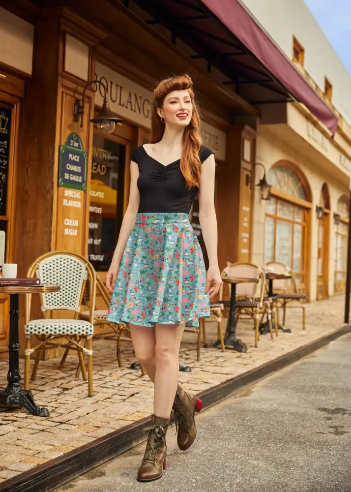 A woman wears a teal colorful fish print vintage a line skater skirt paired with a black sleeveless top