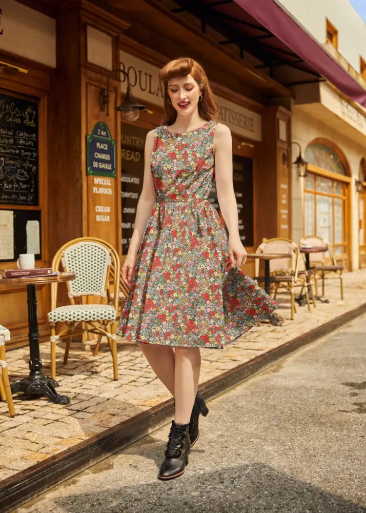 A woman wears a vintage 1950s sleeveless painted floral cotton a-line dress with pockets and red and green blossoms