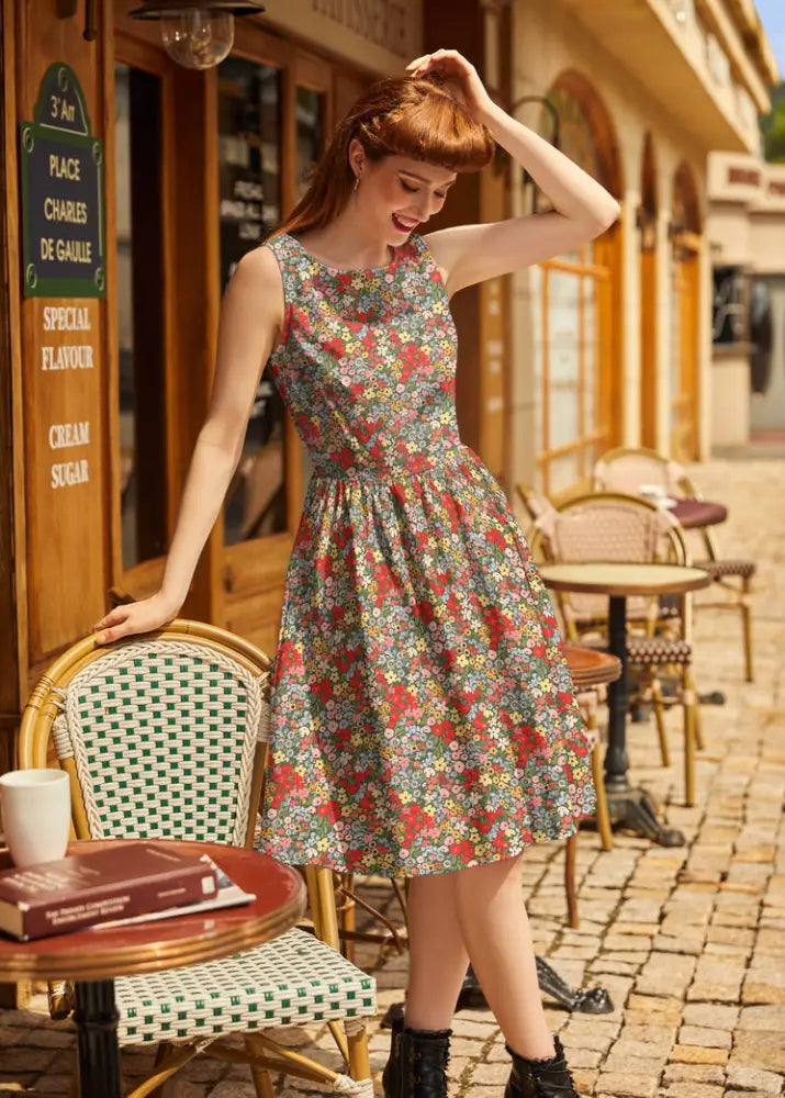 A woman wearing a vintage 1950s painted floral cotton a-line dress with pockets in pastel red green blue and yellow