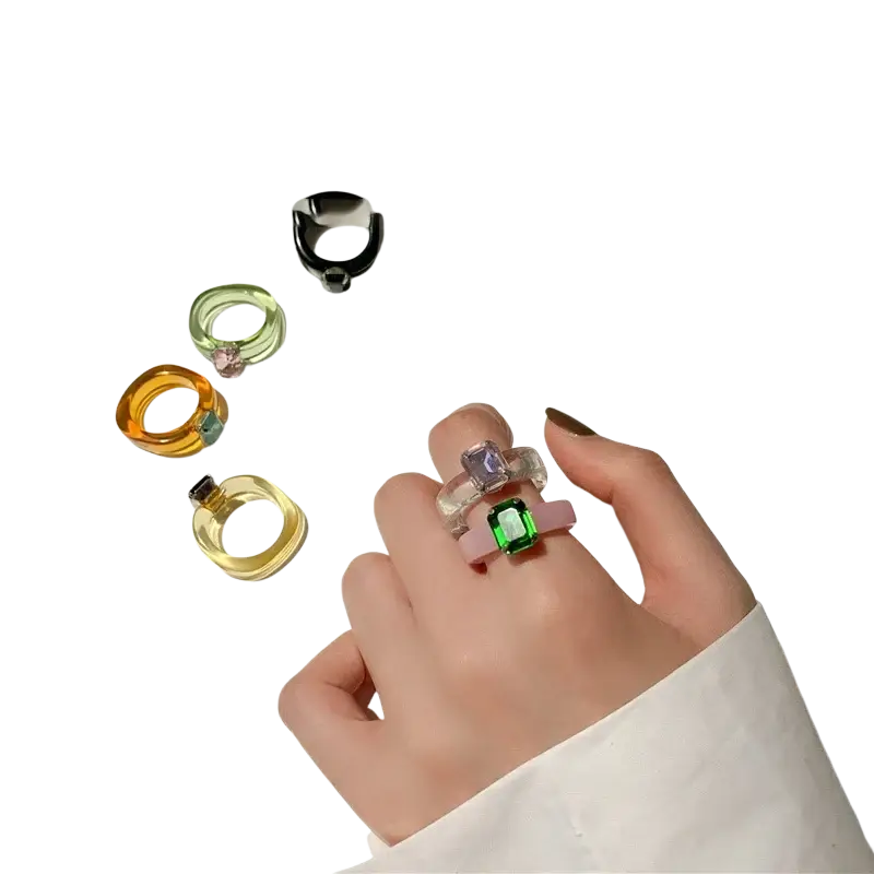 A hand wearing a colorful resin crystal geometric ring with a vibrant green gemstone set in a pink band