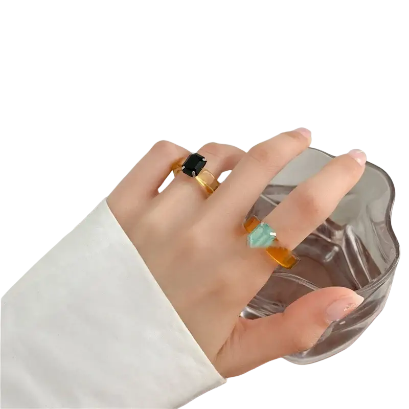 A hand wearing colorful resin crystal geometric rings with black and teal gemstones set in translucent amber bands