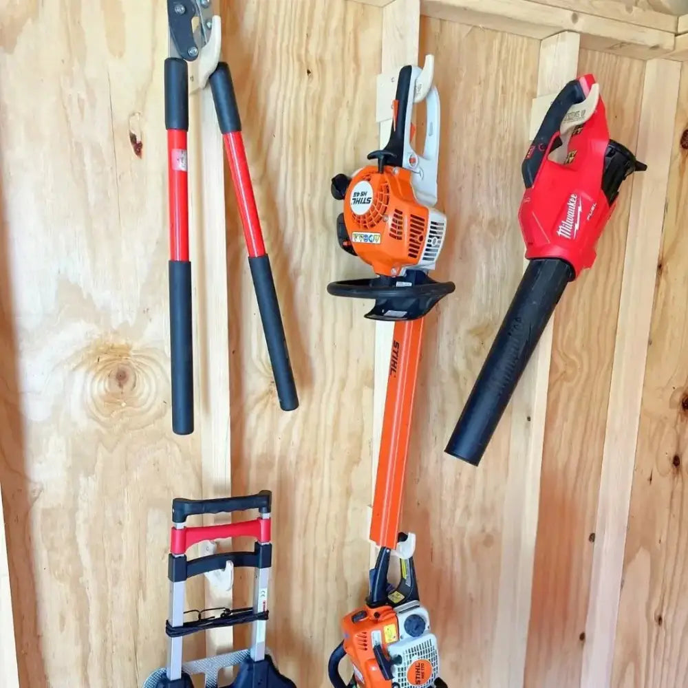 Stud mounted garden tool wall organizer kit with orange and black stihl hedge trimmer with white handle on wood wall