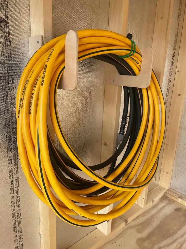 Yellow and black stanley hose neatly coiled on wooden rack in stud mounted garden tool wall organizer kit