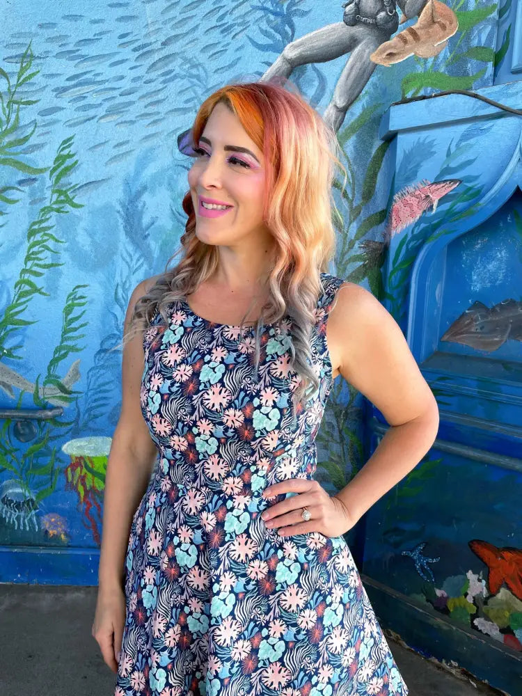 A woman wears a sleeveless navy blue coral floral skater dress with pockets featuring a vibrant pink and light blue pattern